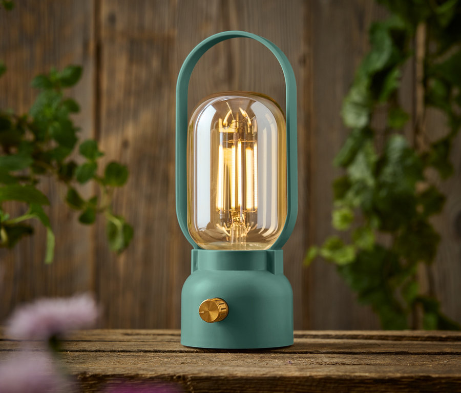 Zelená lampa se zlatým knoflíkem stojí na dřevěném stole.