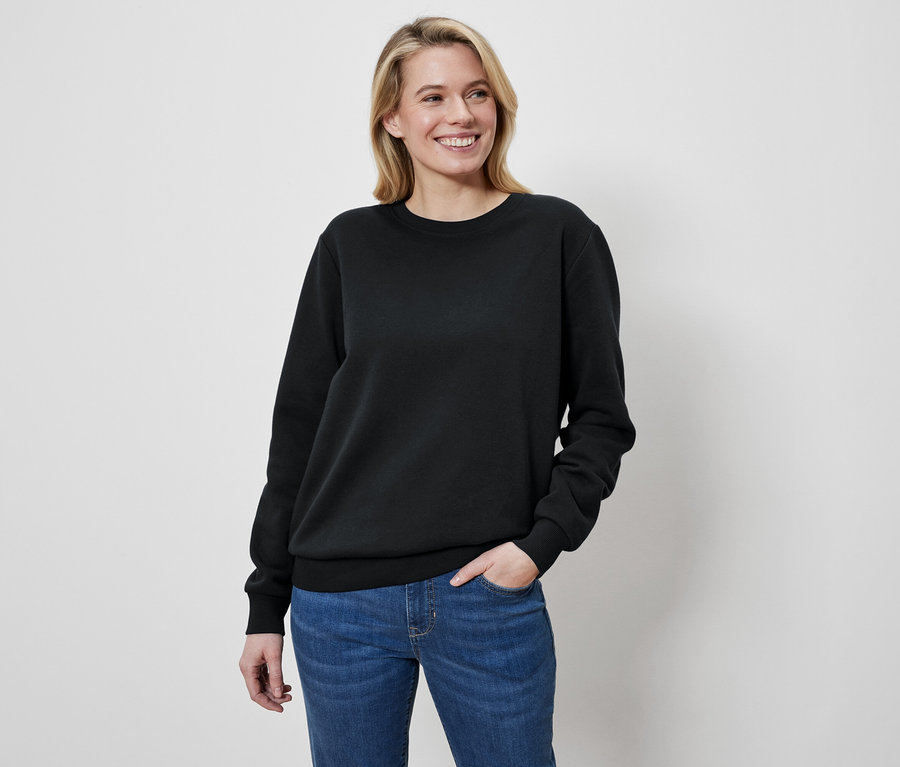 Žena s blond vlasy má na sobě černý svetr a džíny.