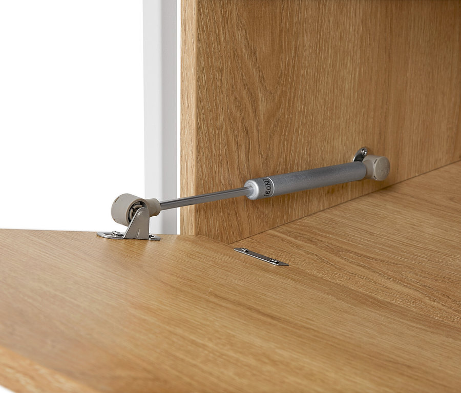 Detailní pohled na nábytkový pant na světle hnědém dřevěném povrchu.