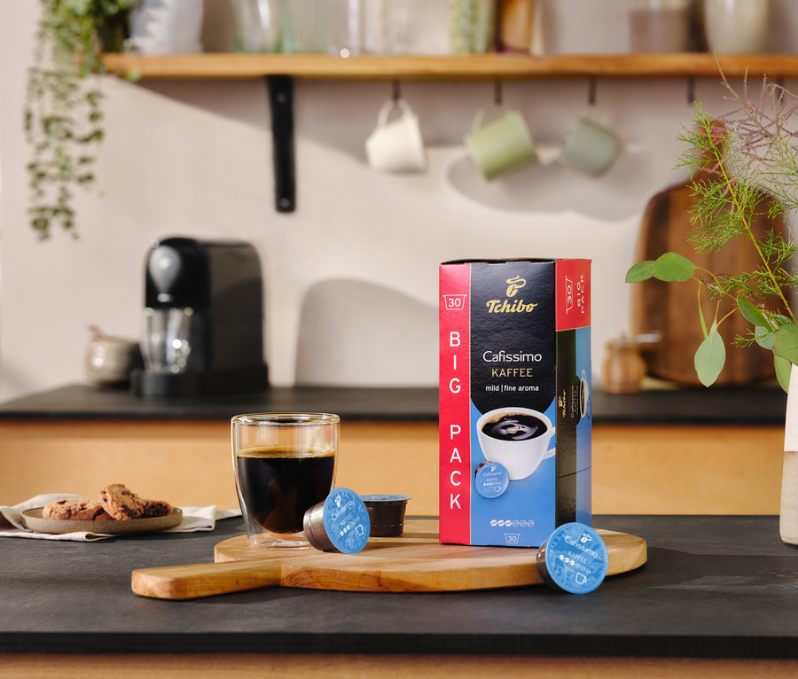Na lince stojí sklenice s kávou vedle balíčku Cafissimo pure+, black a dvou kapslí.