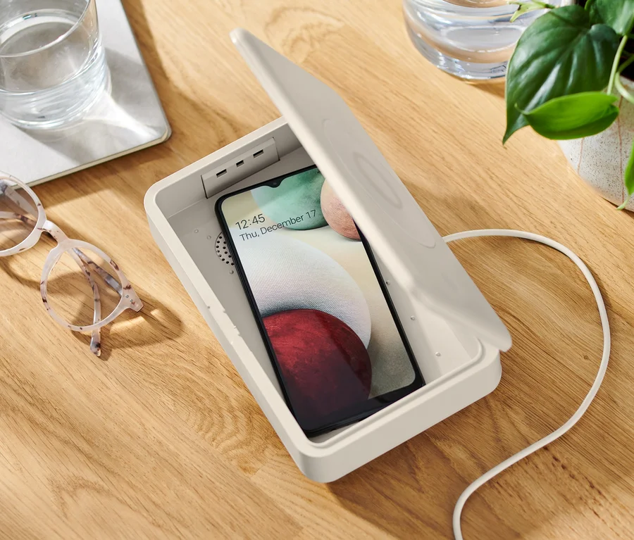 Mobilní telefon je uvnitř otevřeného UV dezinfekčního boxu s bezdrátovým nabíjením.