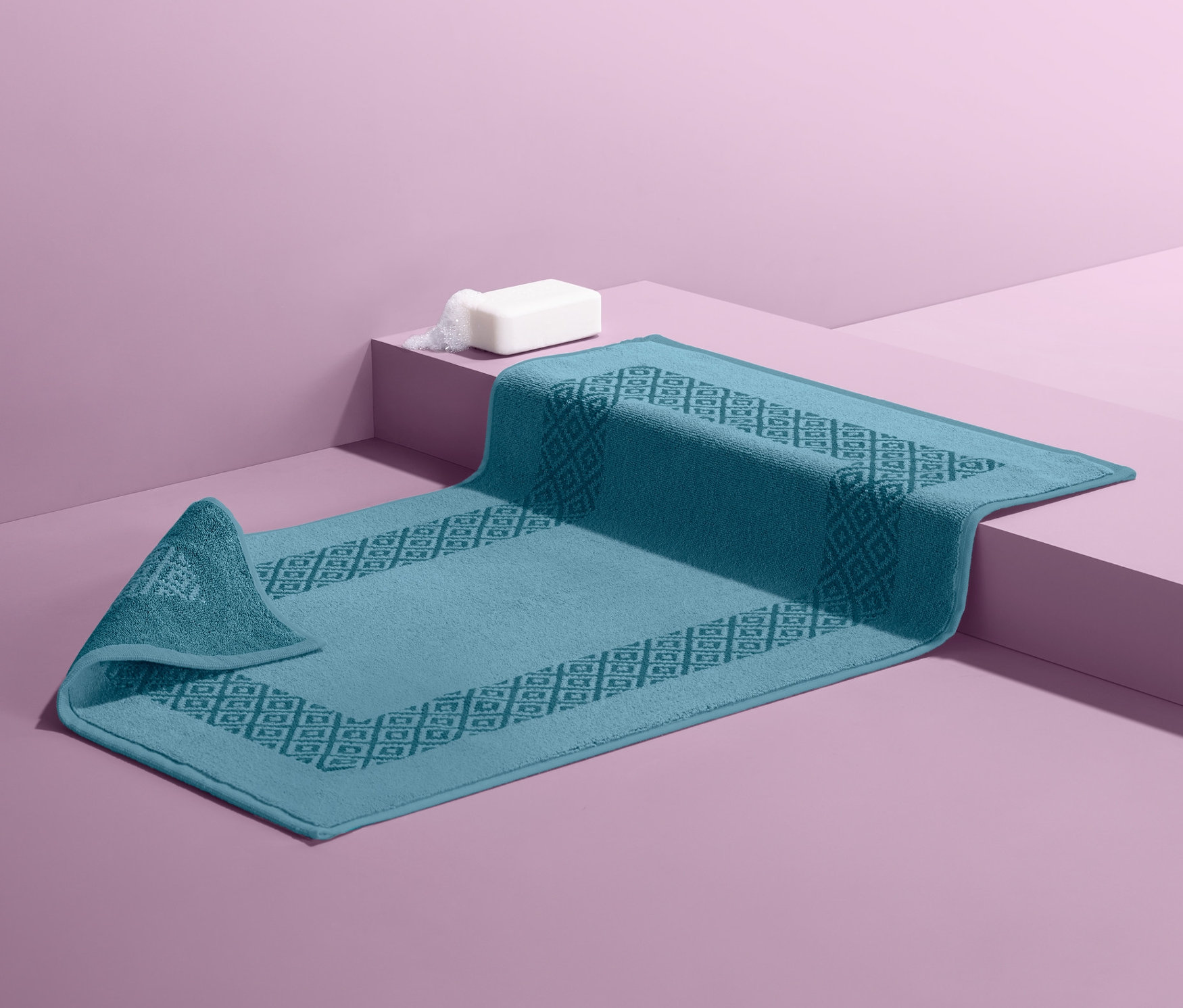 Modrá oboustranná koupelnová předložka na fialovém pozadí.