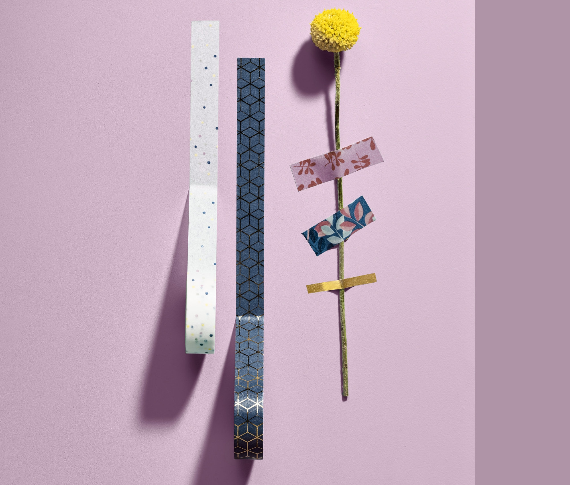 Dvě role dekoračních pásek a žlutý květ s lepicími páskami na stonku.