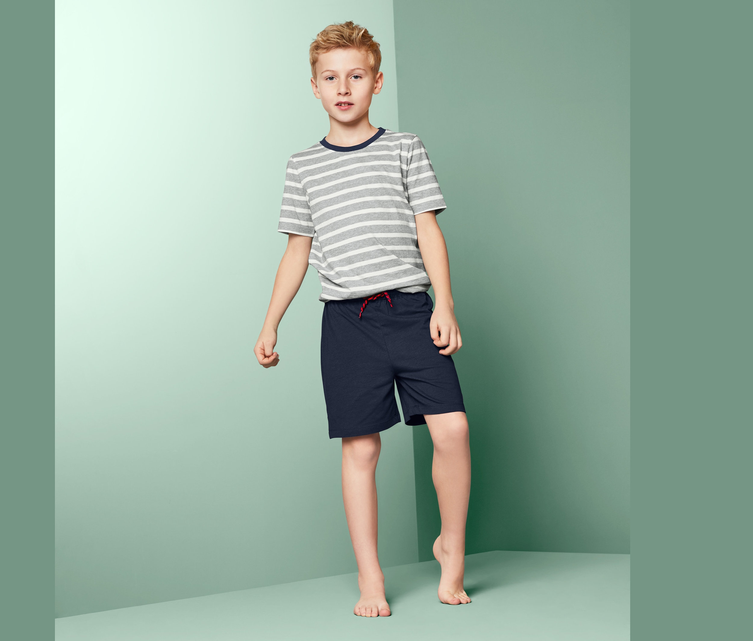 Chlapec stojí na plošině a má na sobě chlapecké krátké pyžamo.