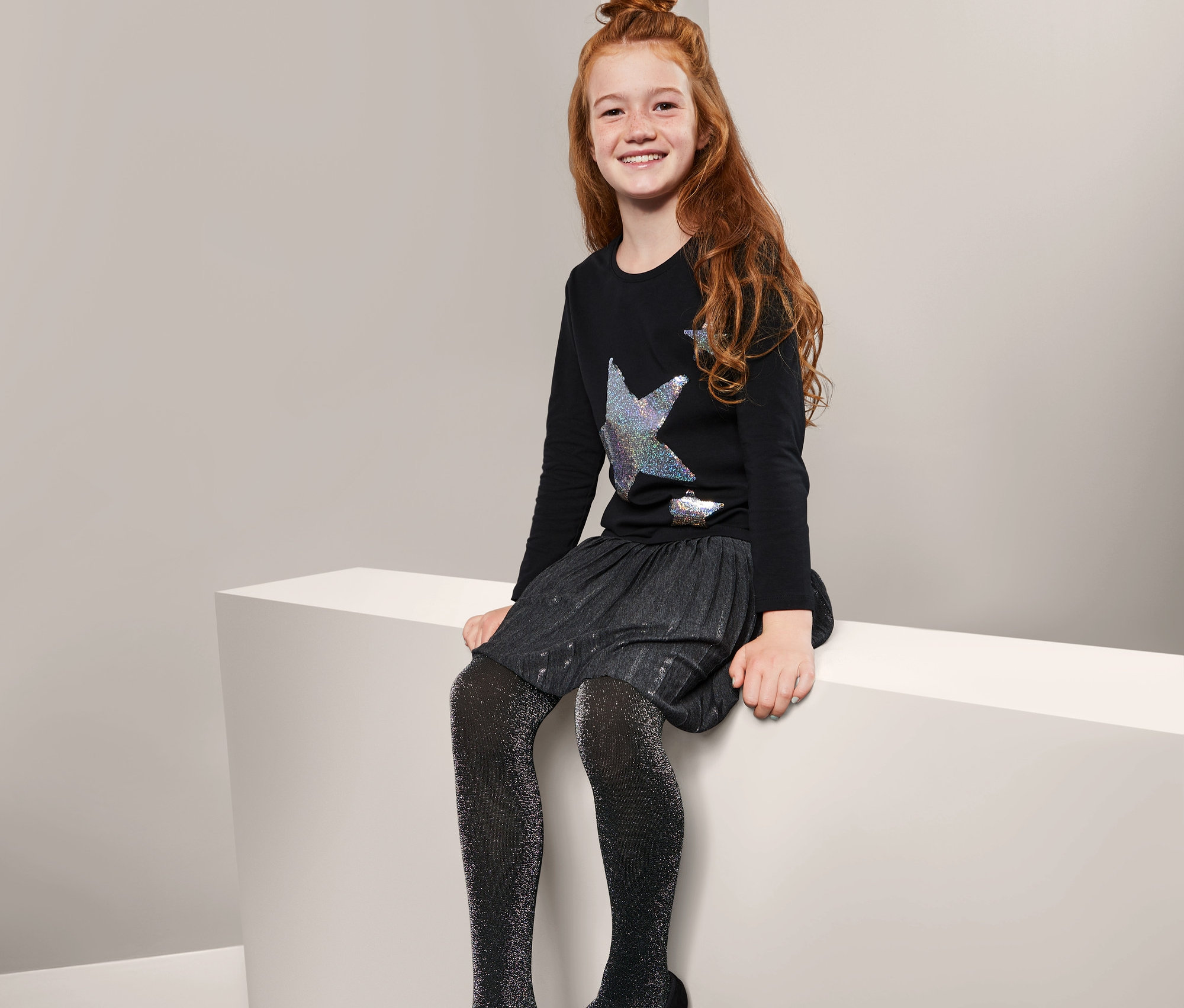 Dívka sedí na bílém kvádru a má na sobě třpytivé punčocháče, 2 ks.