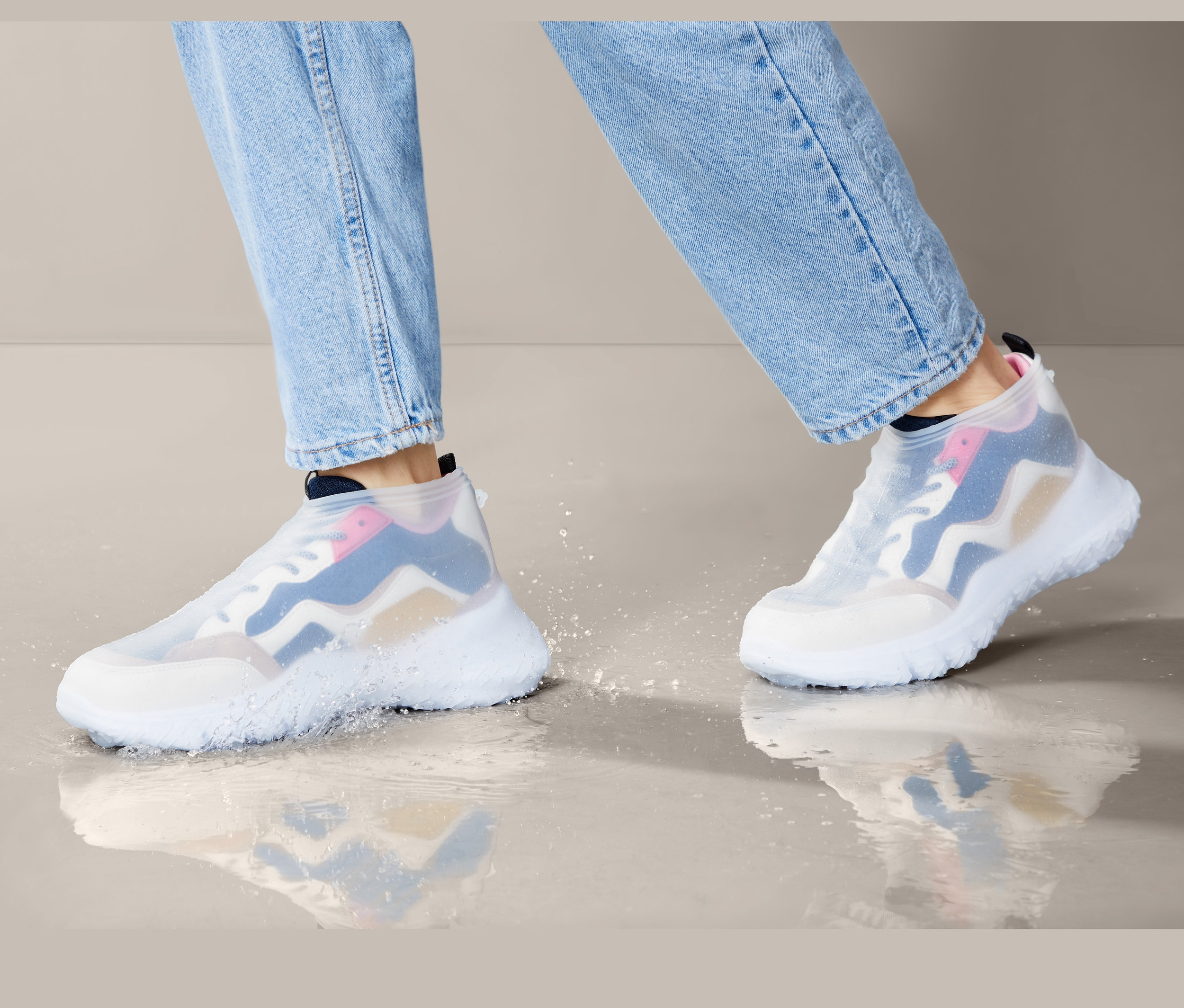 Nohy v džínách kráčejí v Nepromokavých návlecích přes boty v louži.