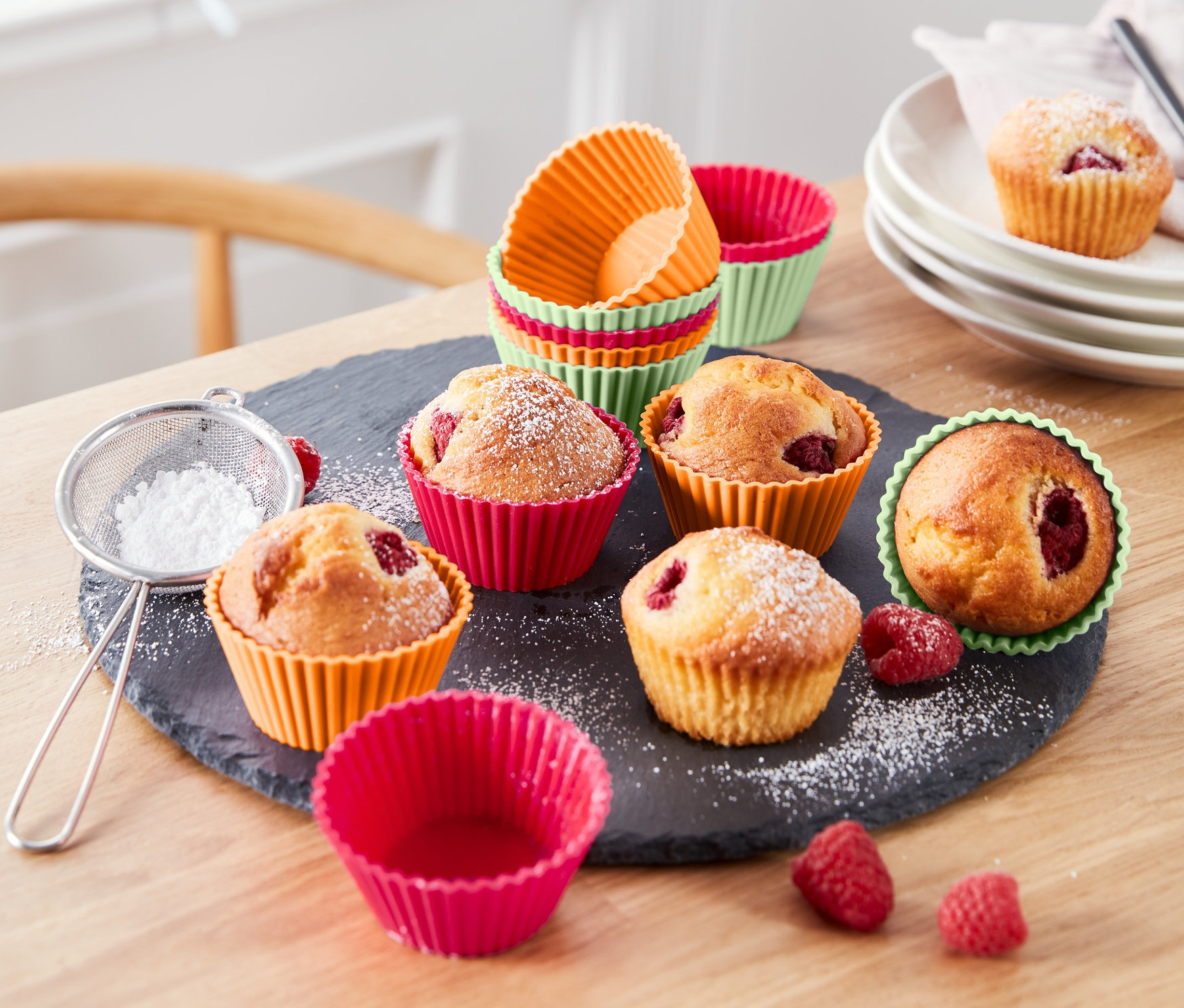 Muffiny v barevných formičkách na muffiny, 12 ks, posypané moučkovým cukrem leží na stole.