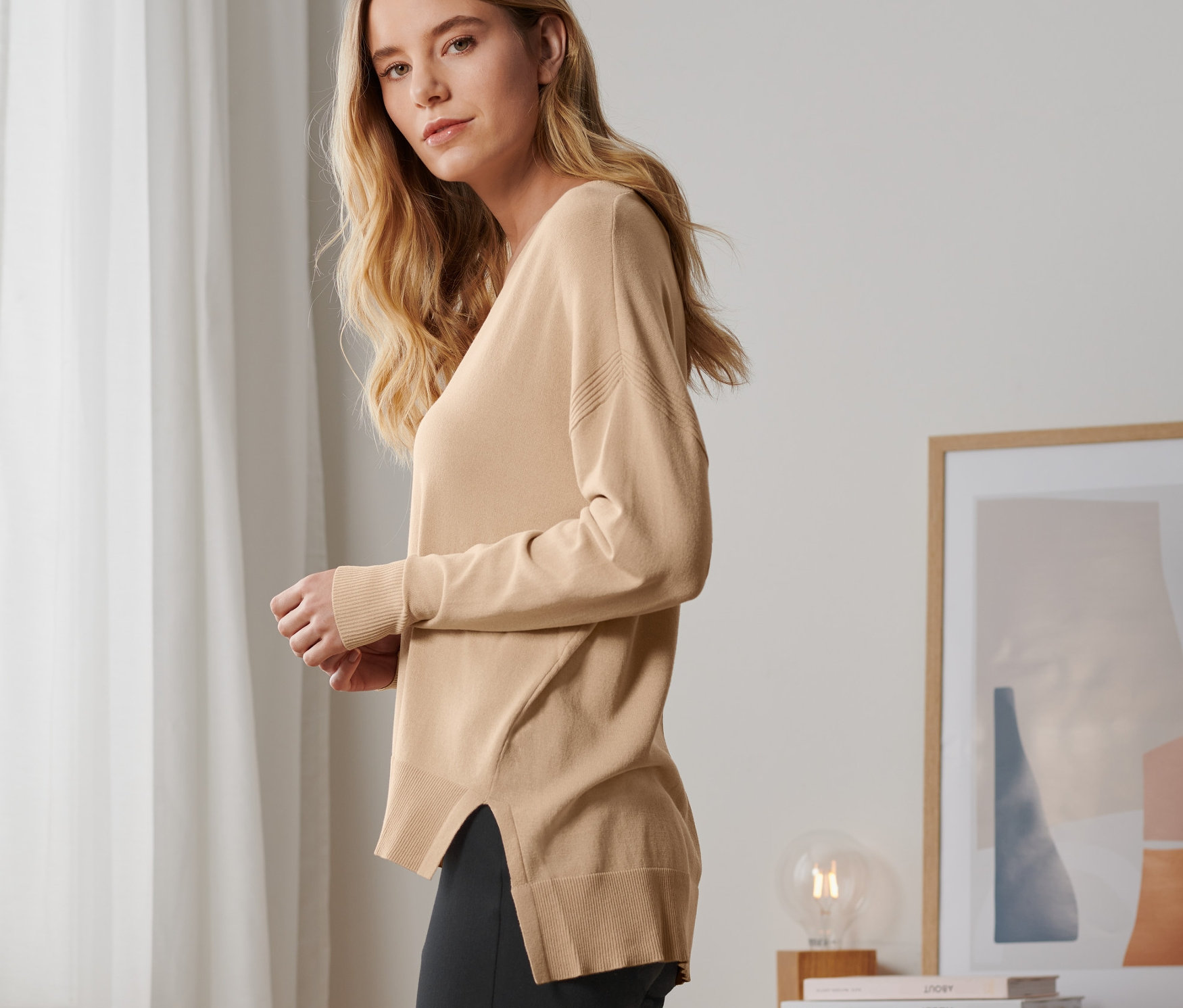 Blondýna pózuje v béžovém svetru z jemné pleteniny a černých kalhotách.