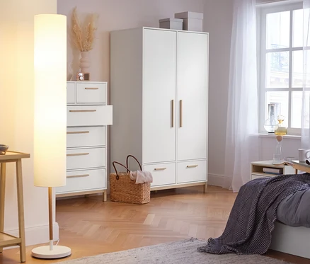 V ložnici stojí konzolový stolek se 2 odkládacími plochami, stojací lampa s textilním stínítkem, vysoká skříňka »Eklund« se zásuvkami a šatní skříň »Eklund« se zásuvkami.