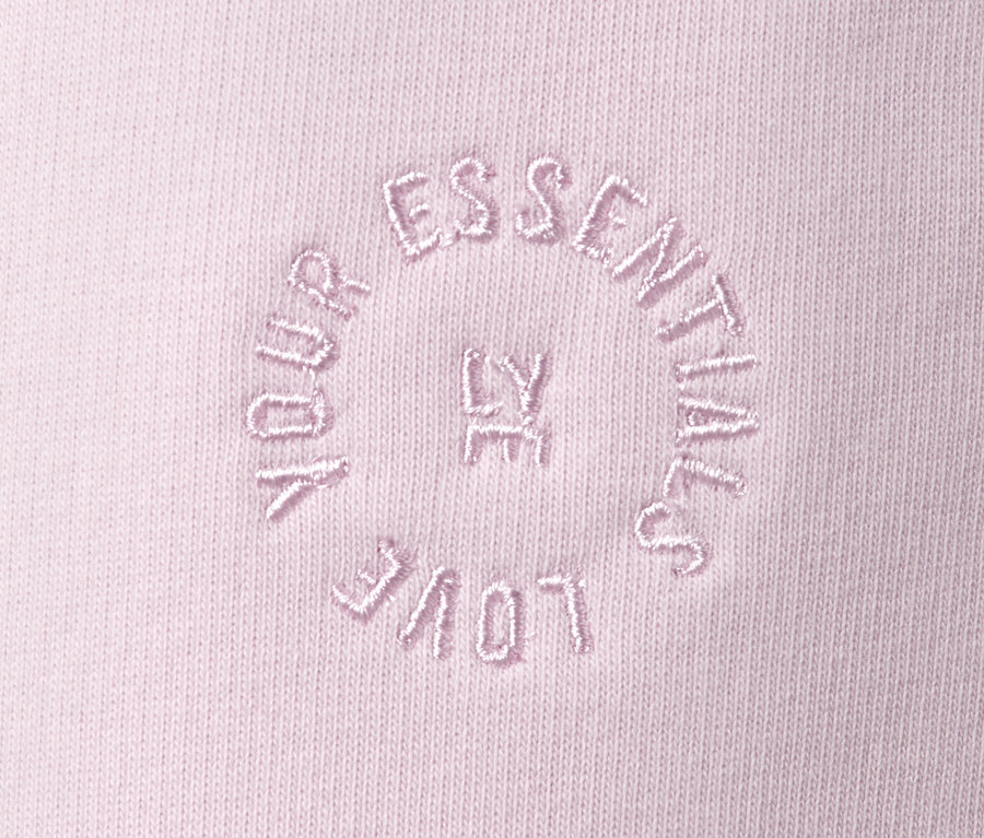Detail růžových tepláků s vyšitým nápisem "YOUR LOVE ESSENTIALS".