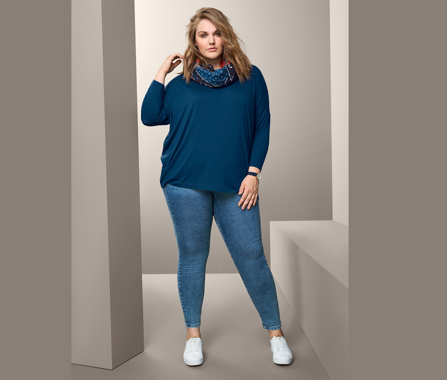 Žena pózuje v modrém oversized triku, kruhové šále a treggínách.