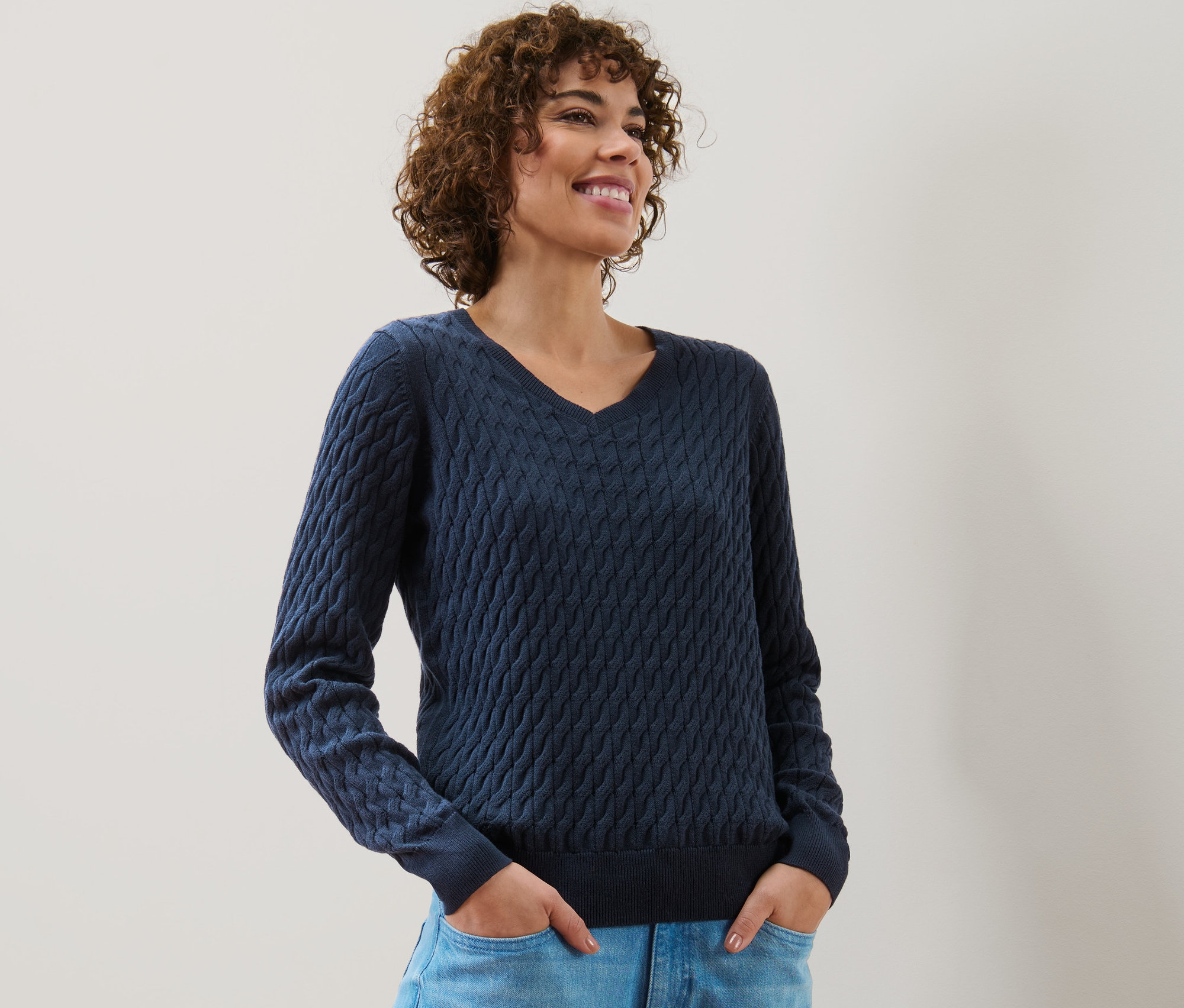 Žena má na sobě tmavě modrý svetr s copánkovým vzorem.