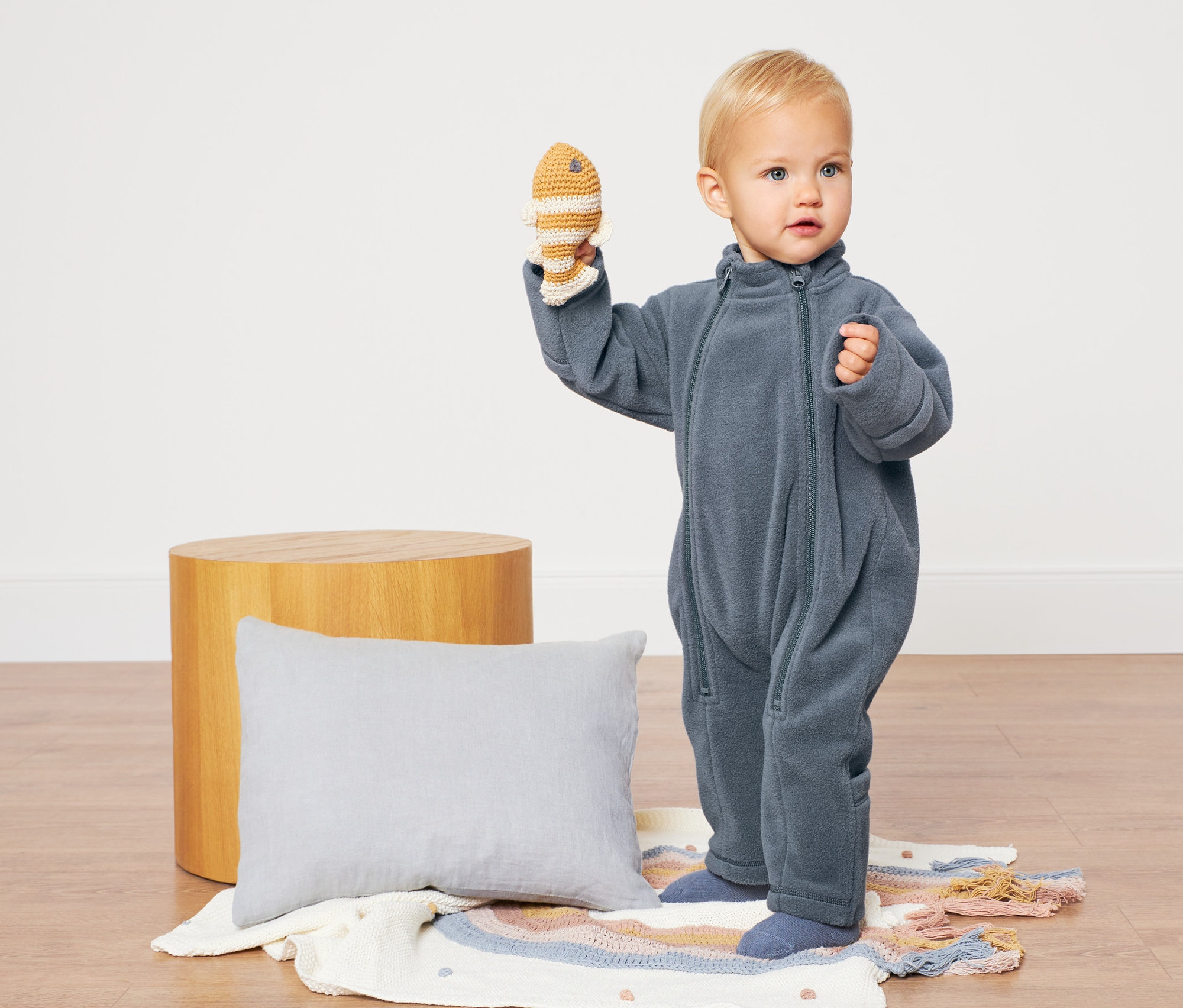 Batole v modrém fleecovém overalu drží hračku rybu.