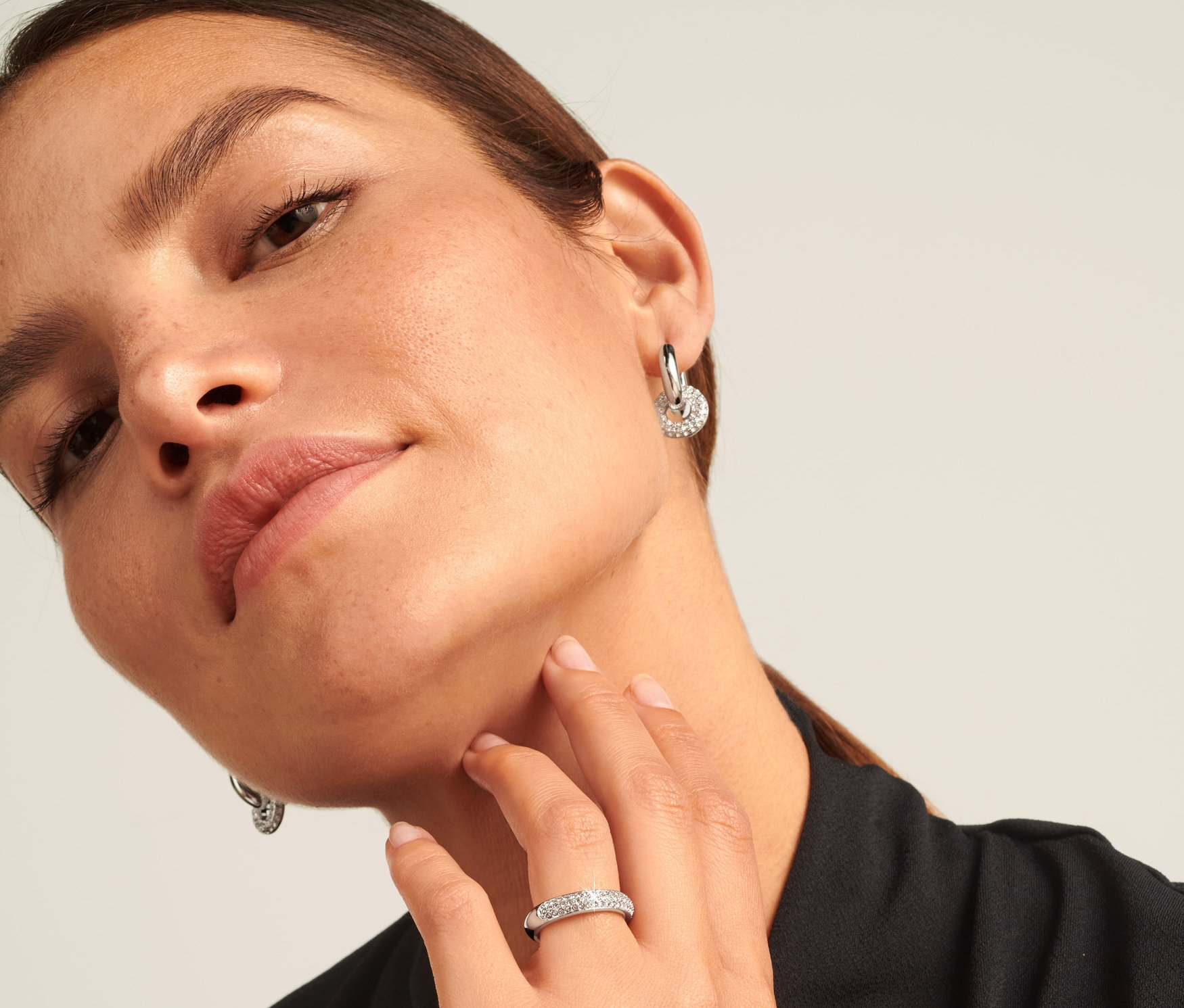 Žena se stříbrným prstenem Sparkle Donut na prsteníčku a náušnicemi.