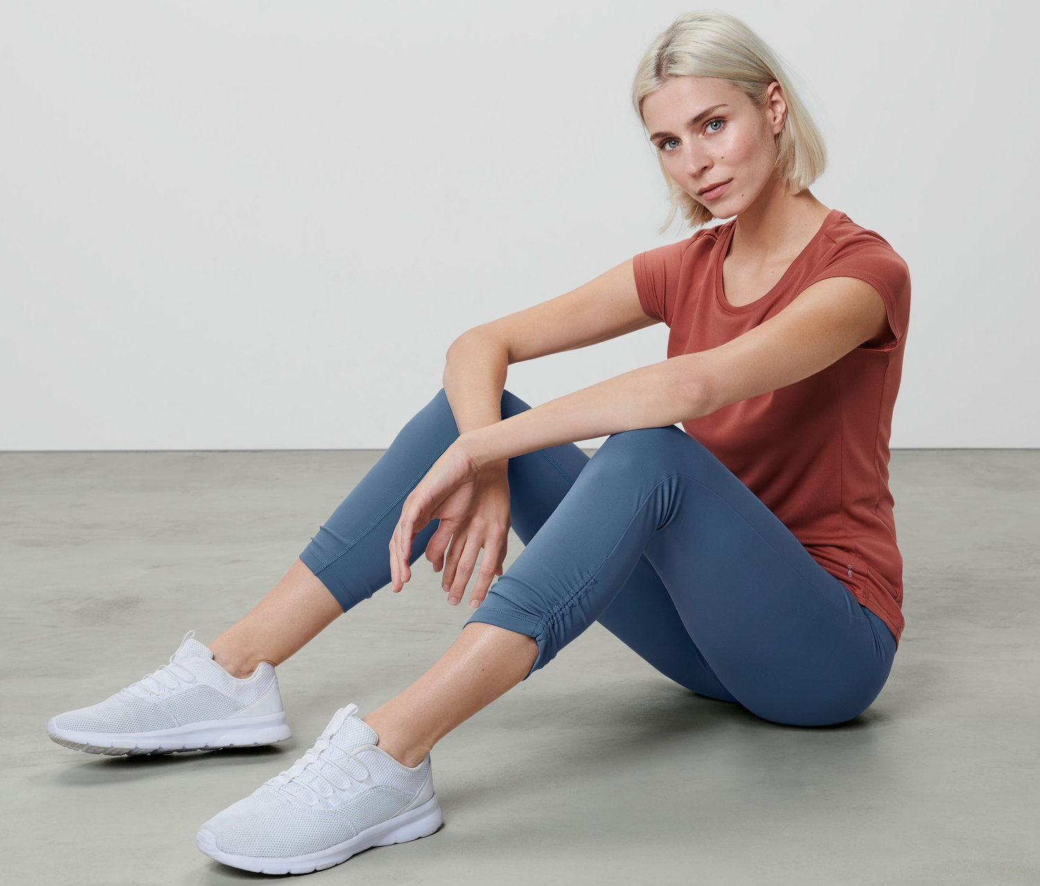 Žena sedí na podlaze v 7/8 sportovních legínách a tričku.