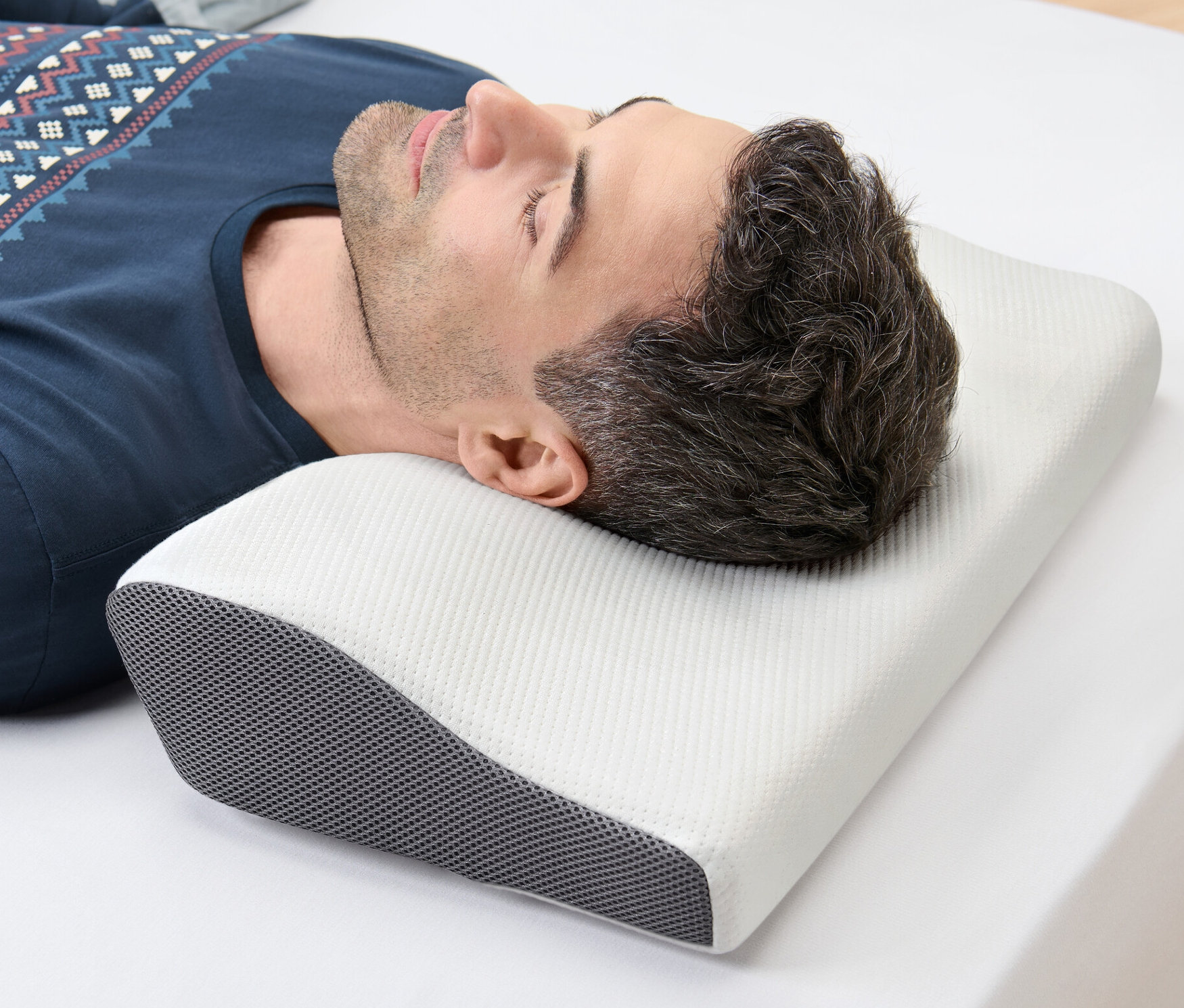 Muž leží na boku na bílém prostěradle a hlavu má na polštáři pro oporu krční páteře.