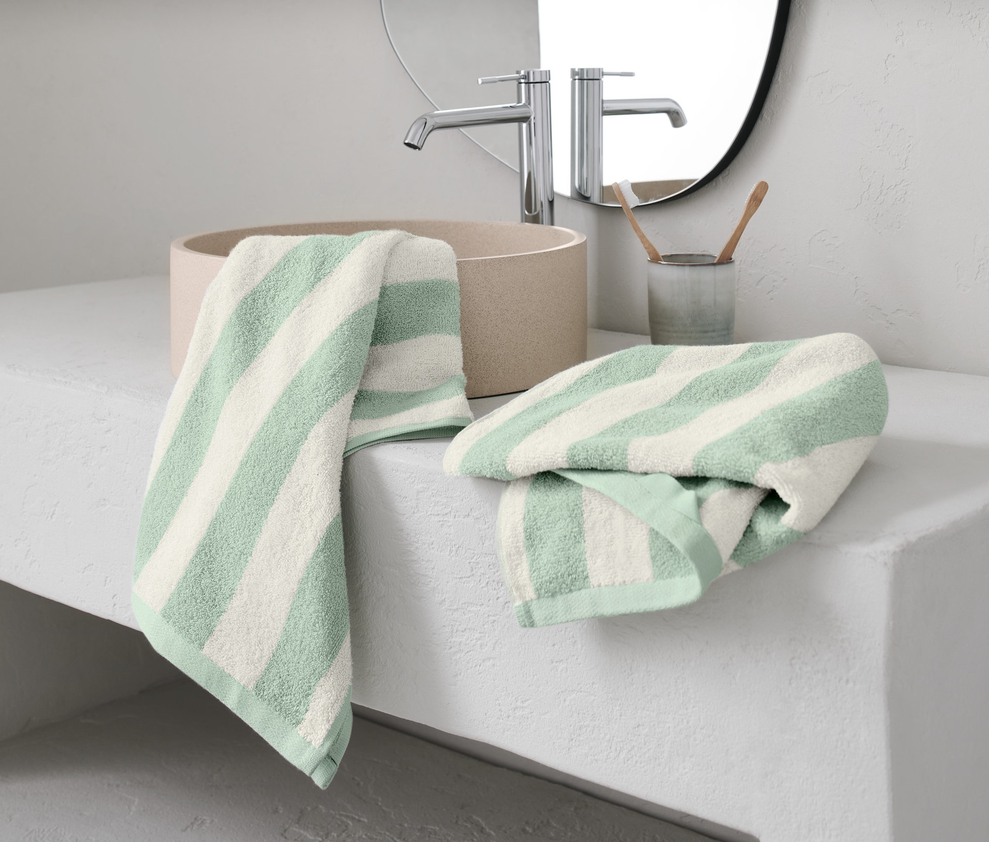 Dva zelené ručníky s proužky leží na umyvadle.