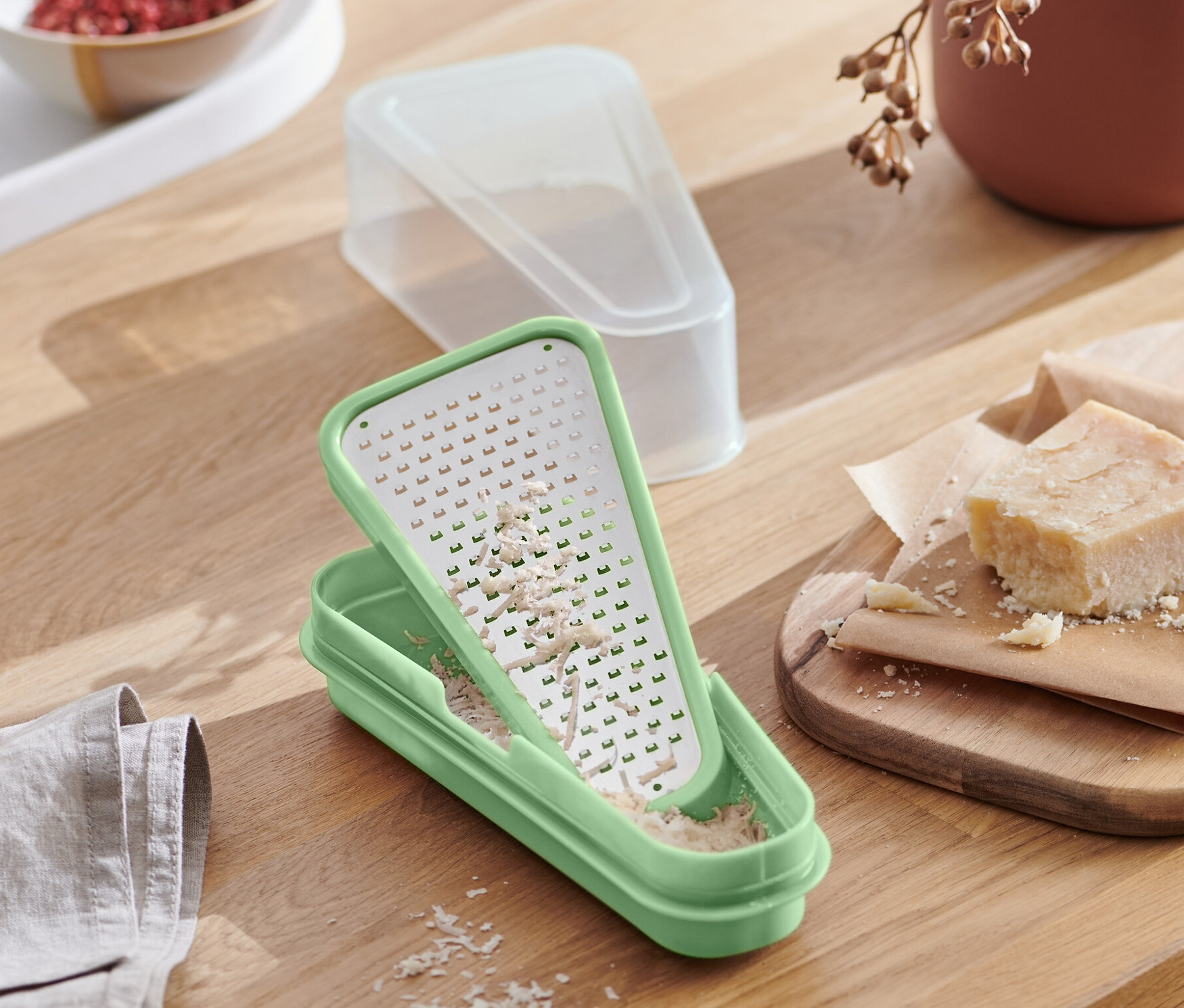 Zelené struhadlo na parmazán 2 v 1 s nastrouhaným sýrem stojí na dřevěném stole vedle talíře těstovin.