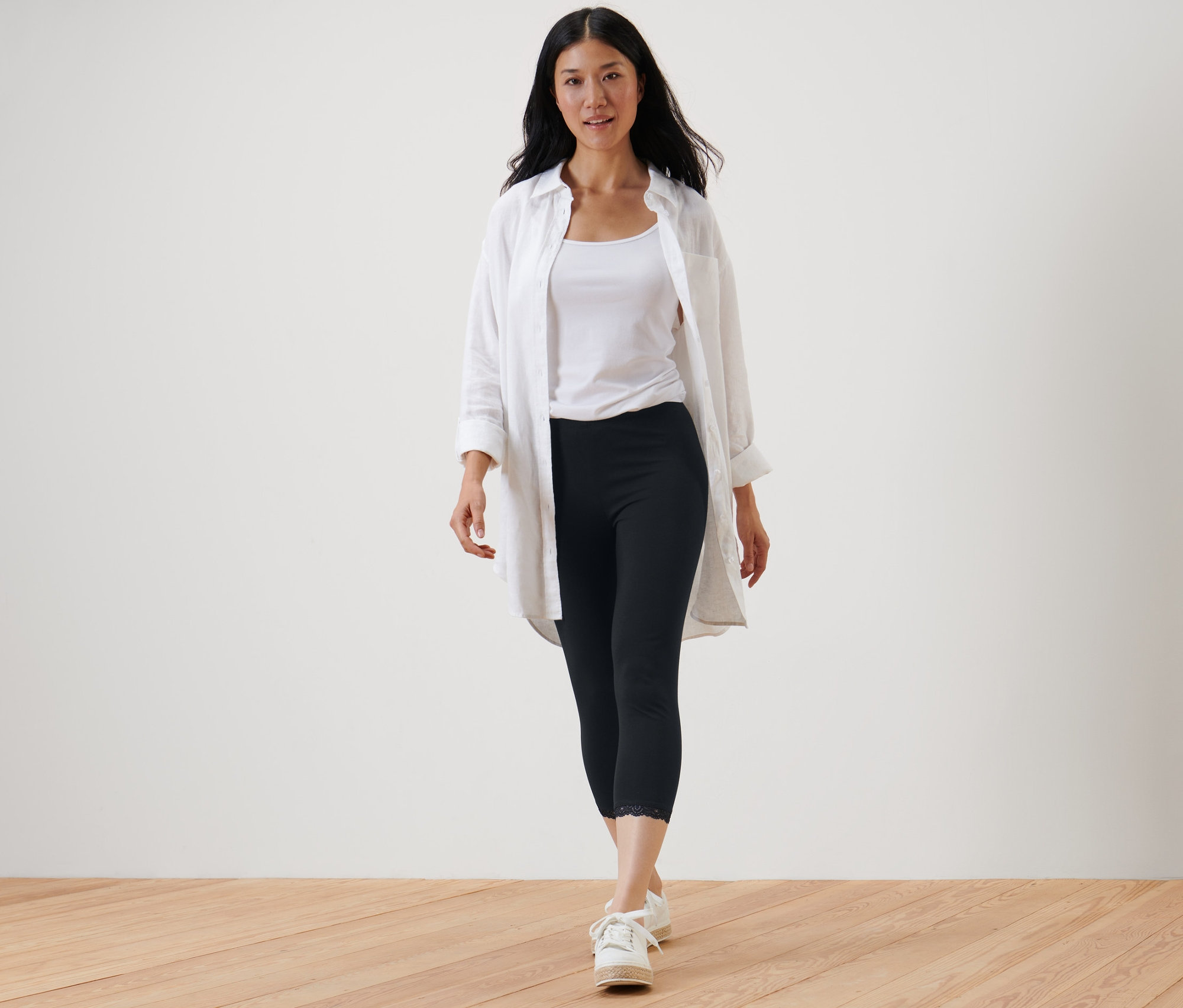 Žena kráčí a má na sobě černé 3/4 legíny s krajkovým lemem, bílé tílko a bílou košili.