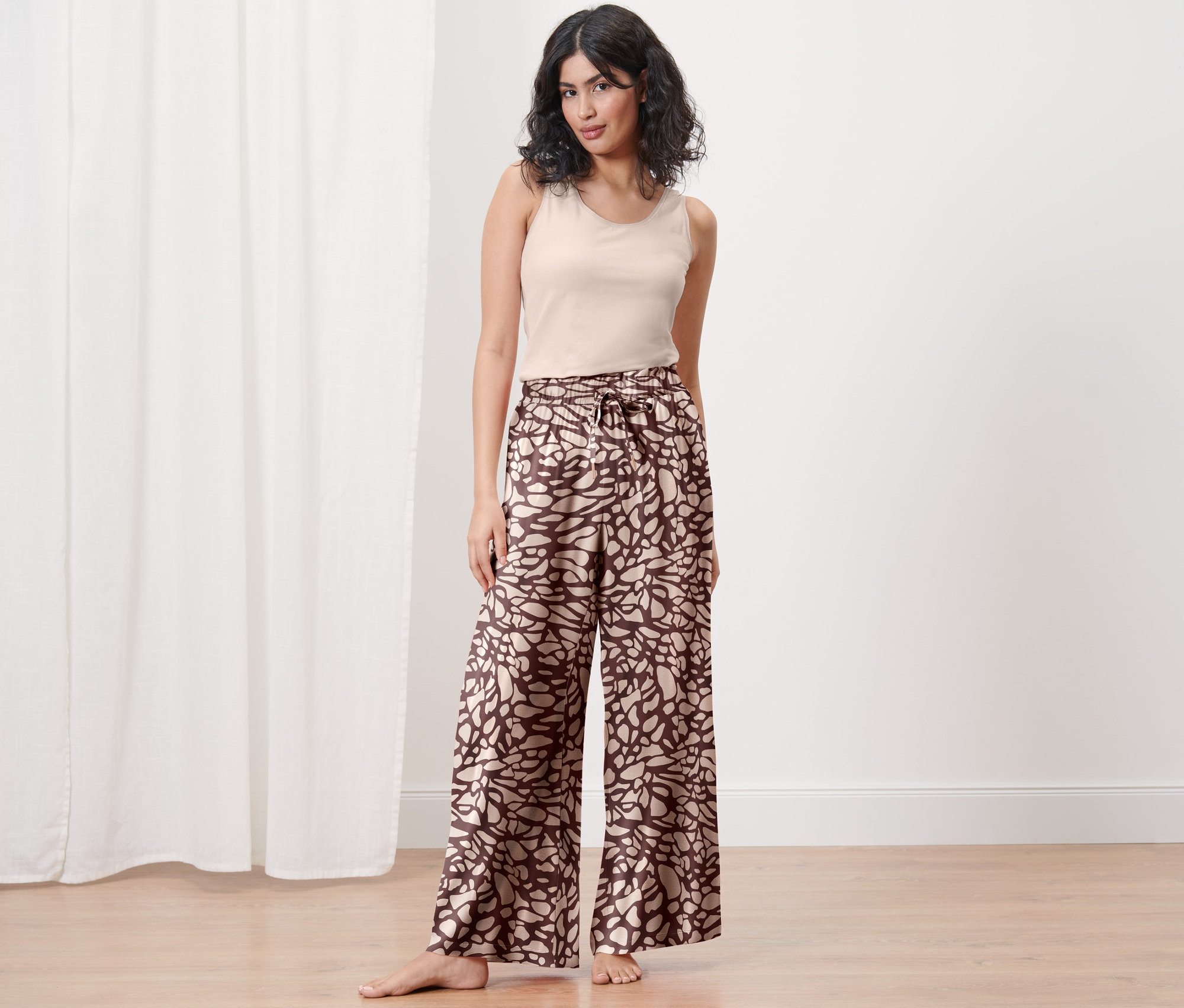 Žena stojí a má na sobě pohodlné kalhoty a tílko.