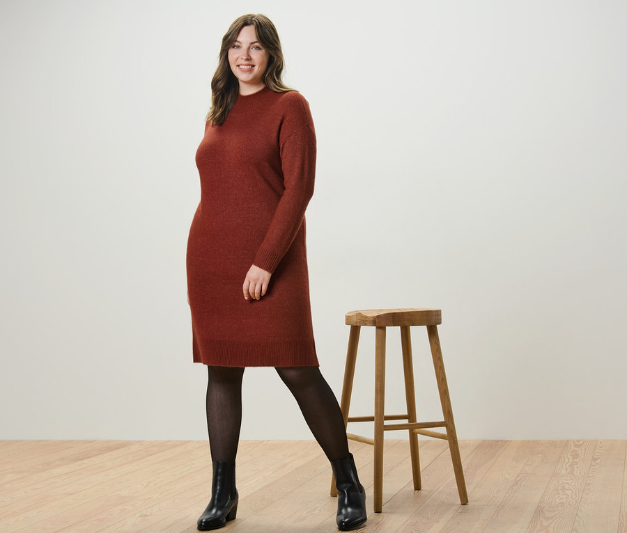 Žena pózuje v pletených šatech s vlnou a jemných průhledných punčocháčích 50 DEN u dřevěné stoličky.