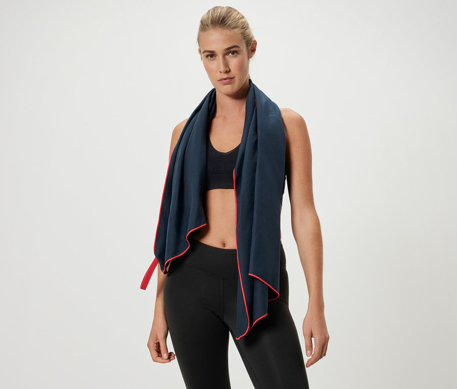 Žena s blond vlasy má kolem krku sportovní ručník s červeným lemováním.