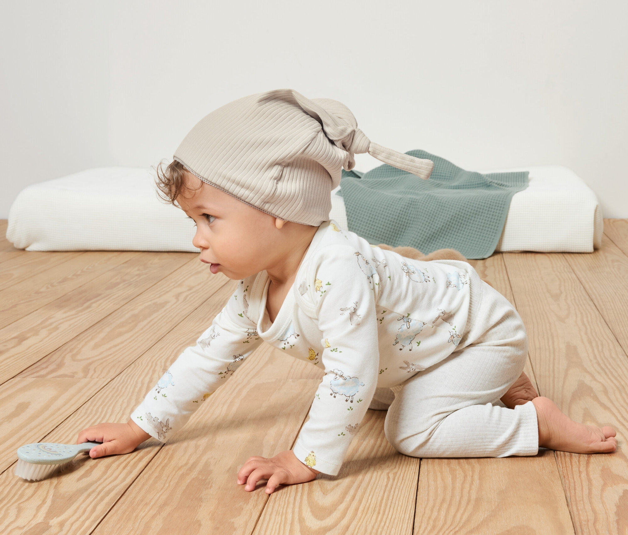 Dítě leze po dřevěné podlaze a má na sobě béžovou žerzejovou čepici.