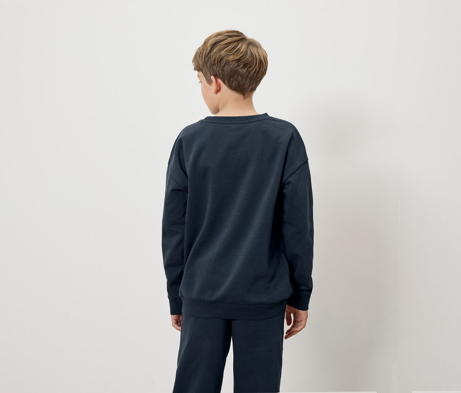 Chlapec v tmavě modré mikině a kalhotách stojící zády k fotoaparátu.