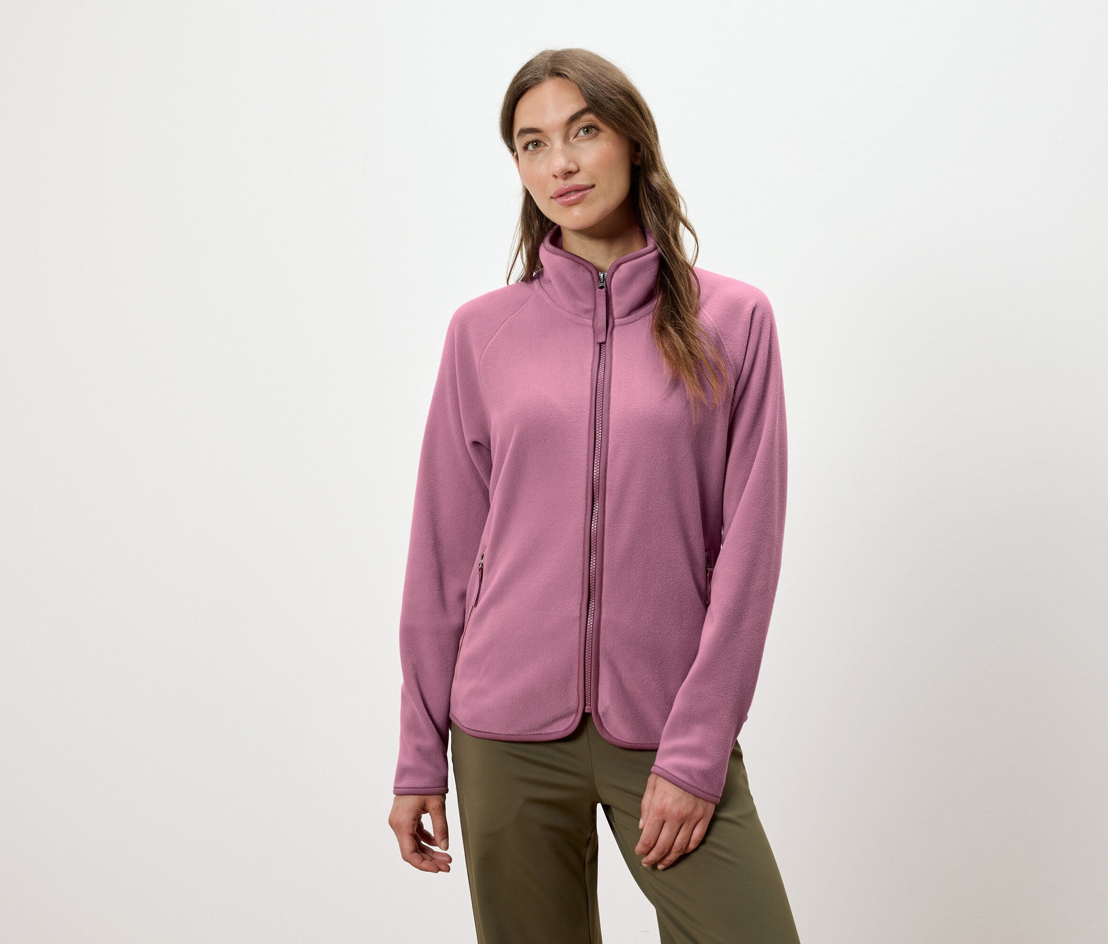 Žena má na sobě růžovou fleecovou bundu na zip a zelené kalhoty.