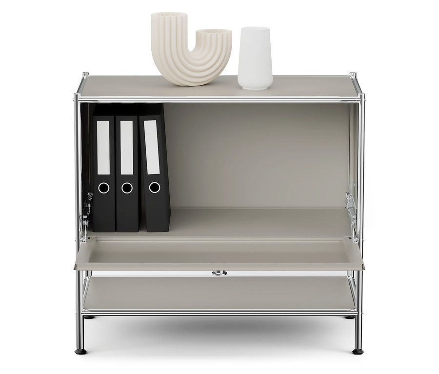 Šedá skříňka s chromovaným rámem, na horní polici jsou dvě bílé vázy a v horní polici jsou tři černé pořadače.