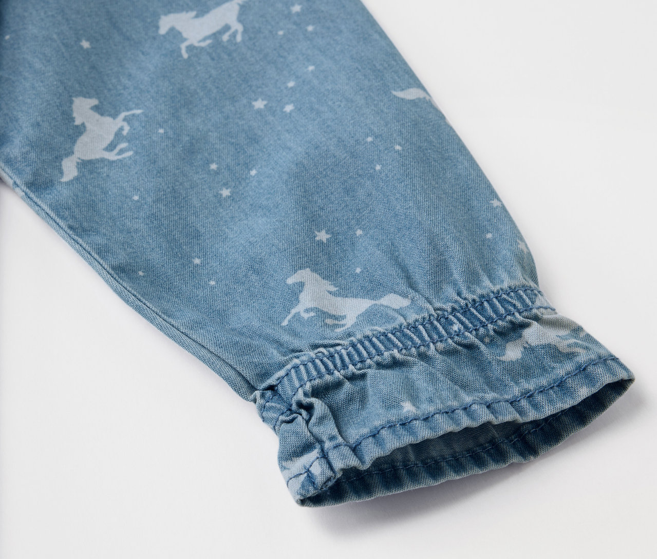 Detail rukávu džínových šatů s potiskem koní a hvězd.