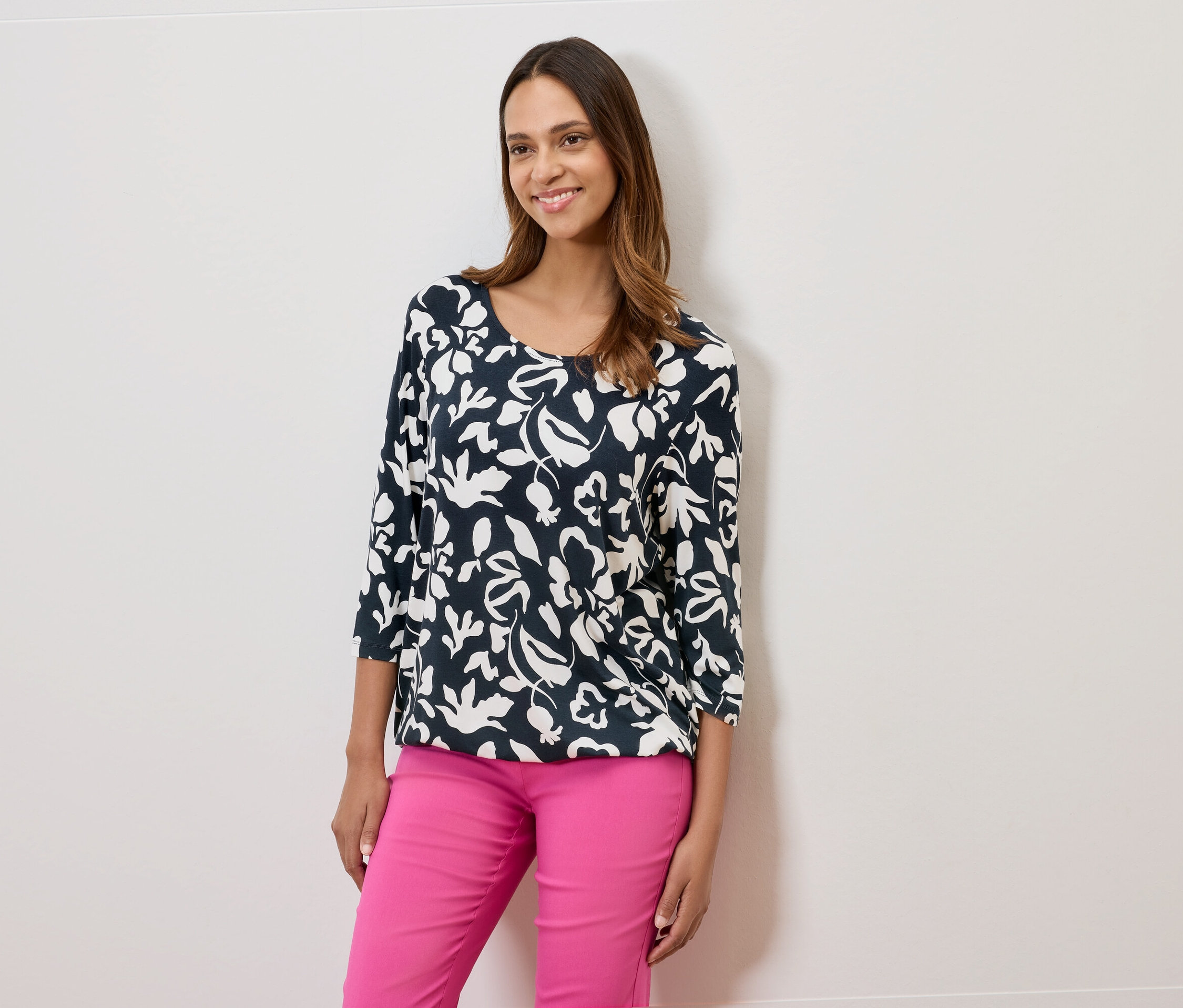 Žena má na sobě tmavě modrou blůzu s květinovým vzorem a růžové kalhoty.