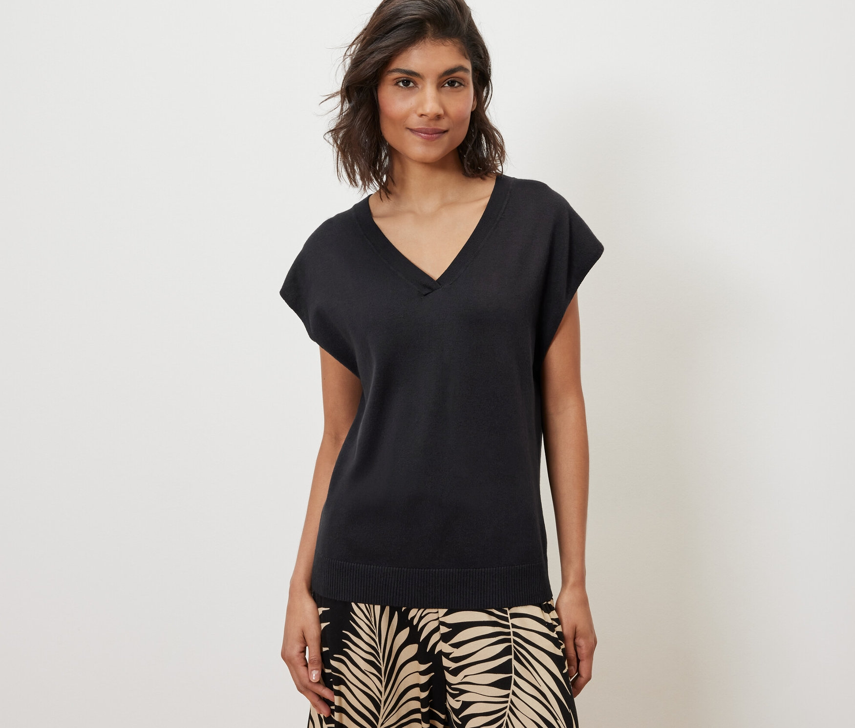 Žena má na sobě černý svetr z jemného úpletu s krátkým rukávem a vzorované kalhoty.