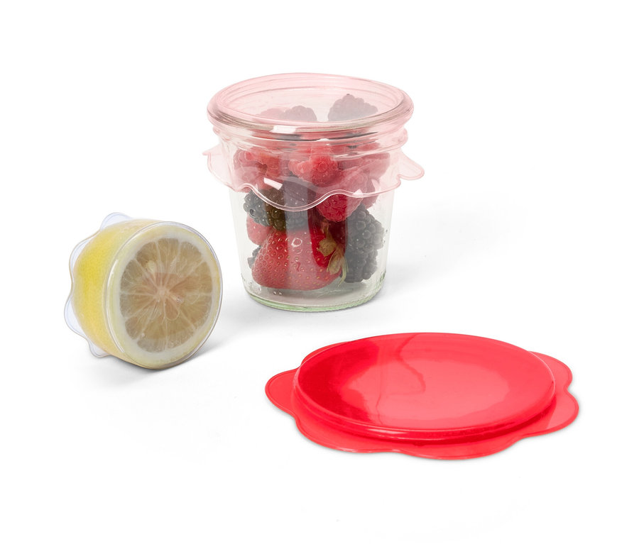 Sklenice s ovocem zakrytá silikonovým víčkem pro uchování čerstvosti, vedle ní půlka citronu zakrytá stejným víčkem a červené víčko.