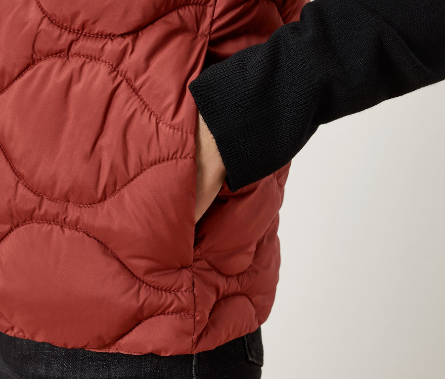 Detailní záběr na osobu v hnědé prošívané vestě s rukou v kapse.