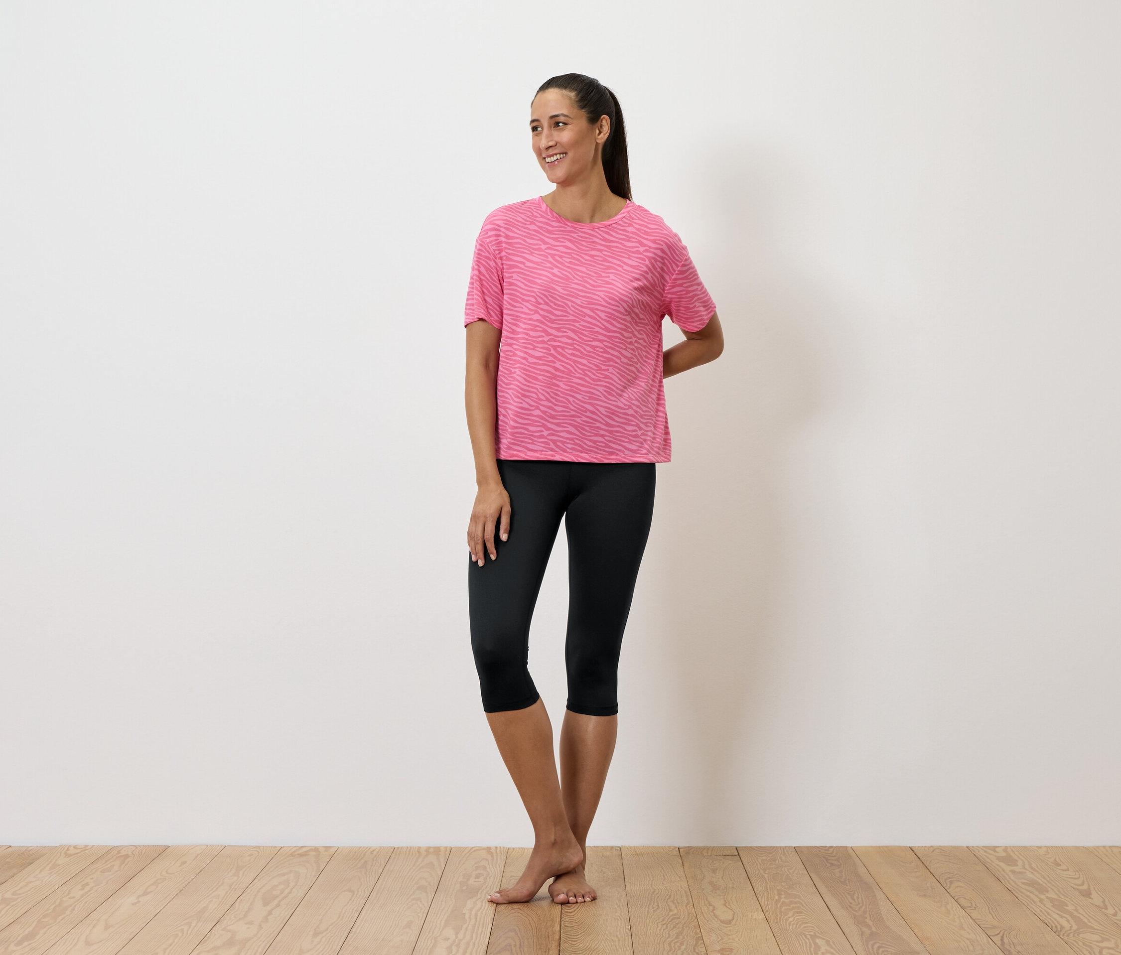 Žena stojí a má na sobě růžové tričko a černé legíny.