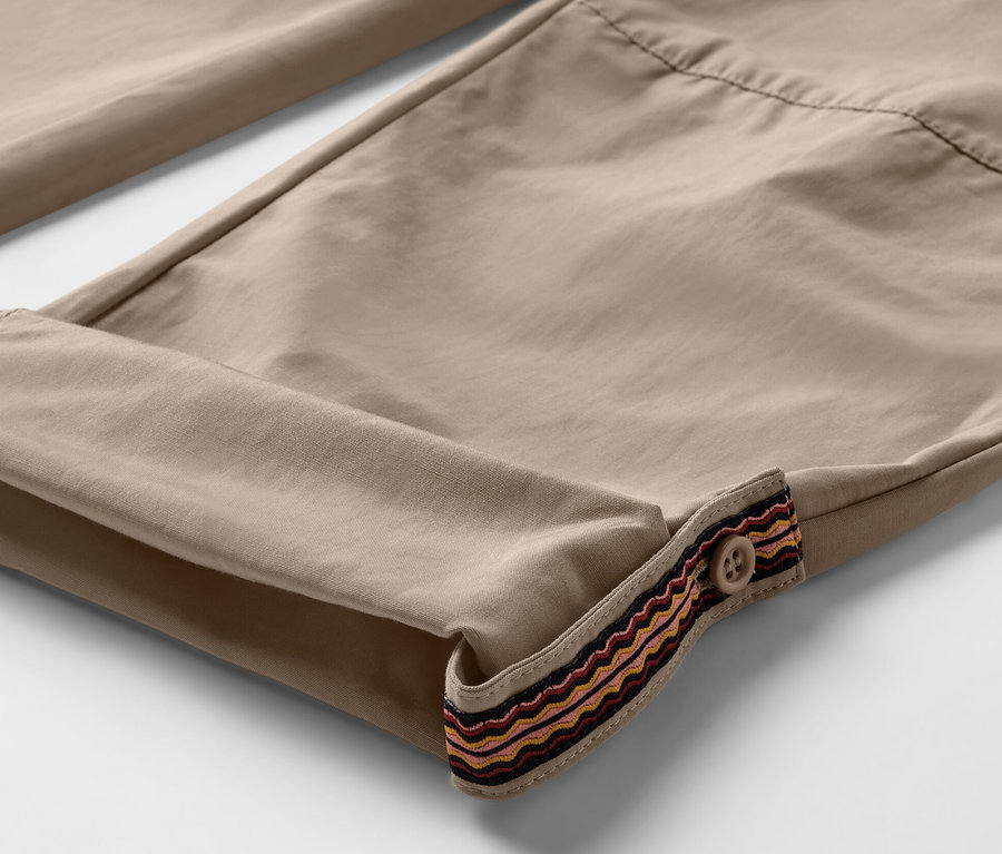 Detail béžových outdoorových kalhot s ohrnutými nohavicemi a ozdobným lemem s knoflíkem. Kalhoty mají ochranu proti komárům.