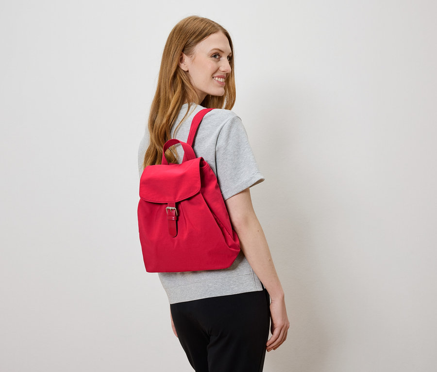 Žena s červeným batohem na zádech se dívá doleva.