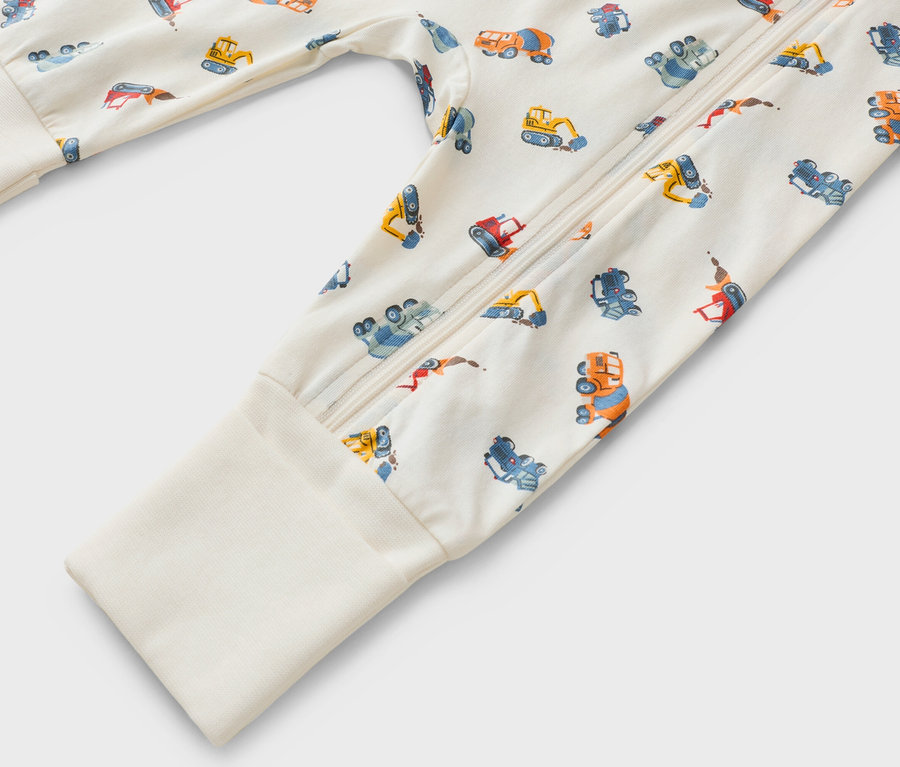 Detailní záběr na overal s dlouhým rukávem, zapínáním na zip a vzorem stavebních vozidel.