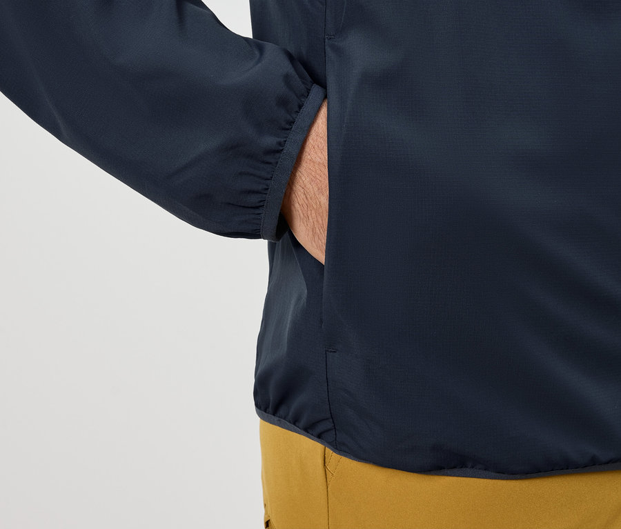 Muž si dává ruku do kapsy tmavě modré bundy.