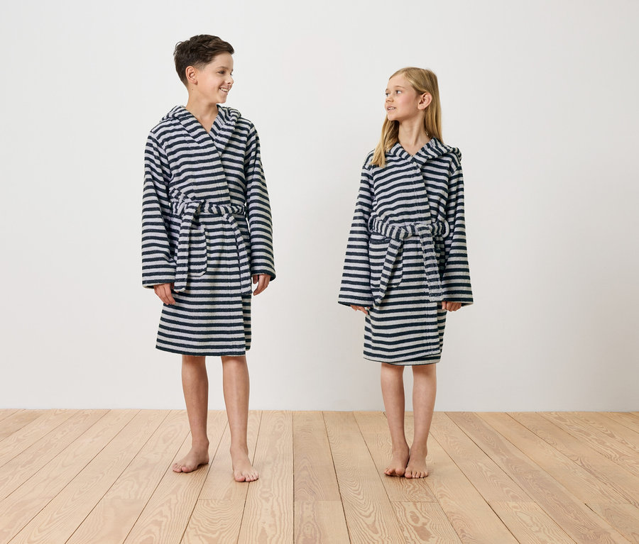 Chlapec a dívka stojí bosí na dřevěné podlaze a mají na sobě pruhované župany s kapucí.