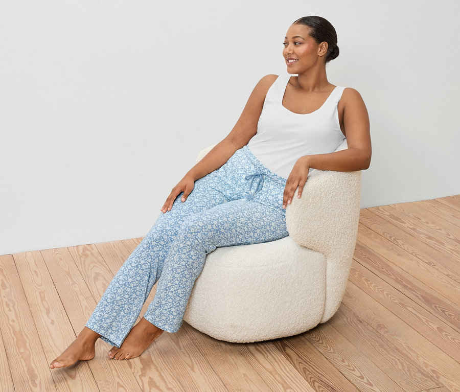 Žena sedí v křesle a má na sobě bílé tílko a modré kalhoty.