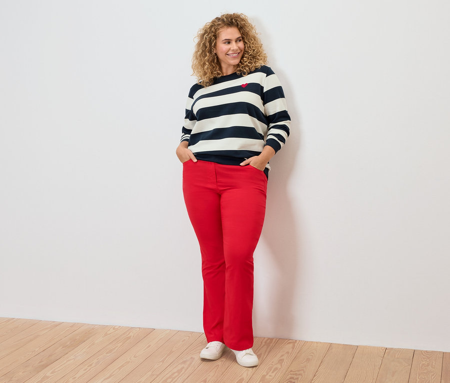 Žena s kudrnatými vlasy má na sobě pruhovaný top a červené kalhoty.