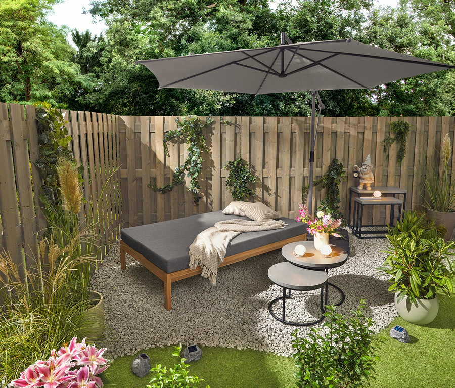 Zahradní lavice 2 v 1, která slouží jako dvojité lehátko, stojí vedle dvou zahradních stolků s polycementovými deskami (průměr cca 50 cm a 60 cm). Zahradní trpaslík s LED lucernou stojí na jednom ze 2 zahradních konzolových stolků s polycementovými deskami. Viditelné jsou také tři dobíjecí stolní lampy a tři prémiové solární LED kameny.