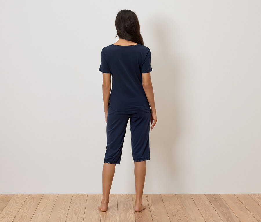 Žena stojí zády ke kameře a má na sobě tmavě modré pyžamo s krajkovým lemem.