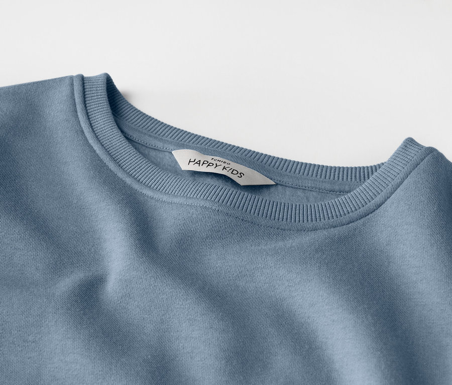 Detailní záběr světle modré dětské mikiny se štítkem s nápisem „HAPPY KIDS“.