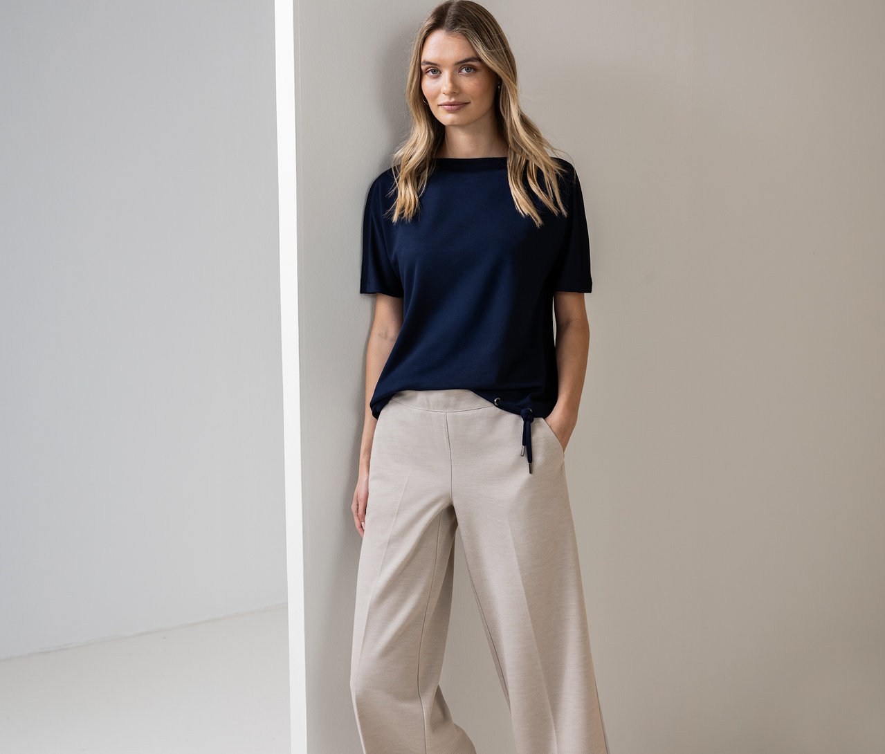 Žena pózuje u zdi v tmavě modrém tričku s krátkým rukávem Street One a béžových kalhotách.