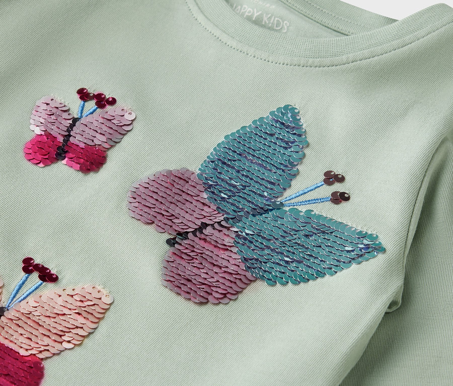 Světle zelené tričko s dlouhým rukávem a flitrovými motýly.