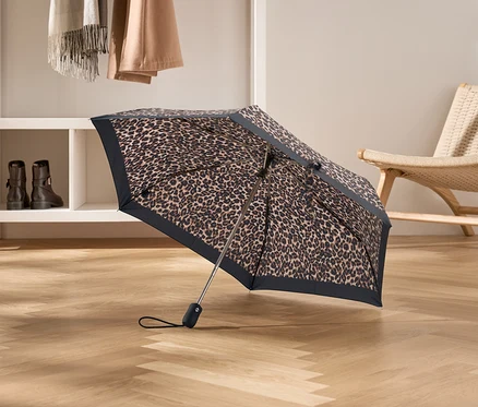 Otevřený deštník s leopardím vzorem stojí na dřevěné podlaze.