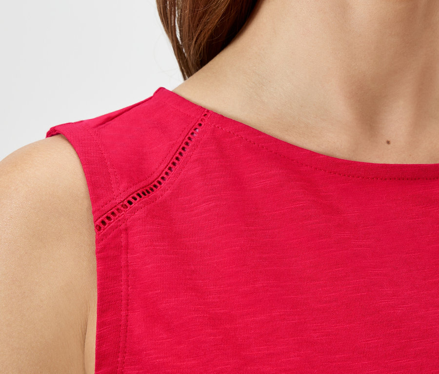 Detailní záběr ženy v červeném topu bez rukávů s dírkovaným vzorem na ramenou.